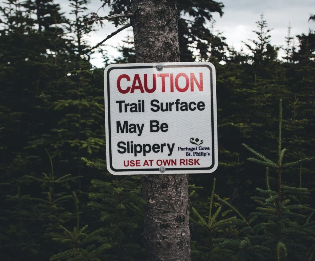 Small footing warning sign on a trail where firm dirt meets loose gravel